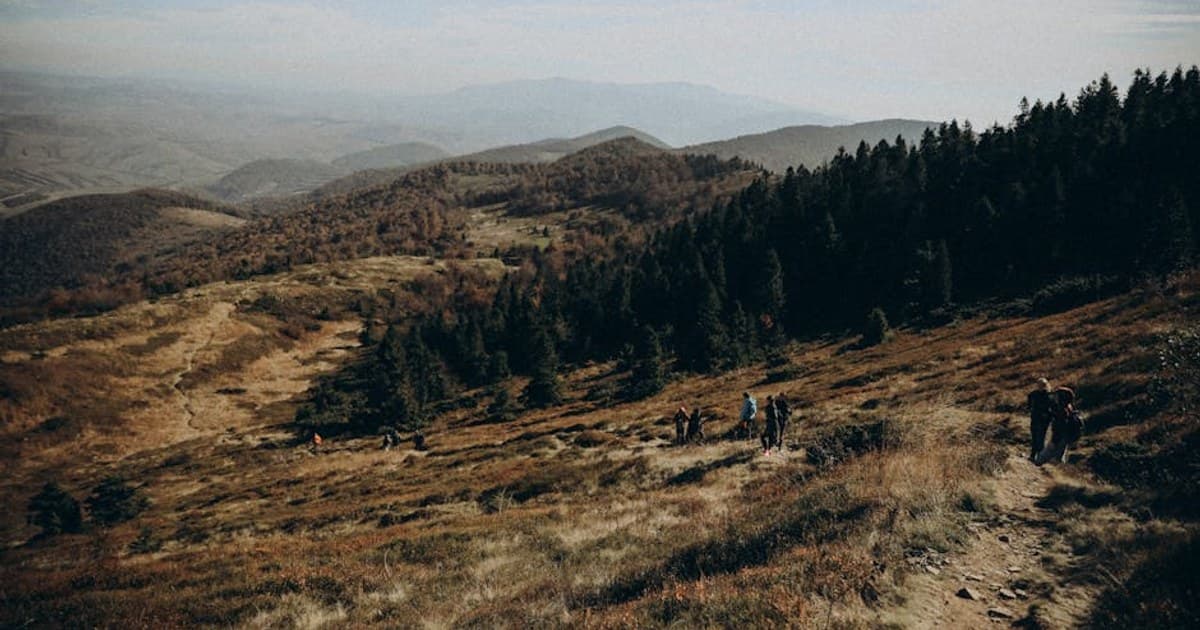Hikers enjoying a scenic mountain trail in autumn, surrounded by forest and rolling hills.