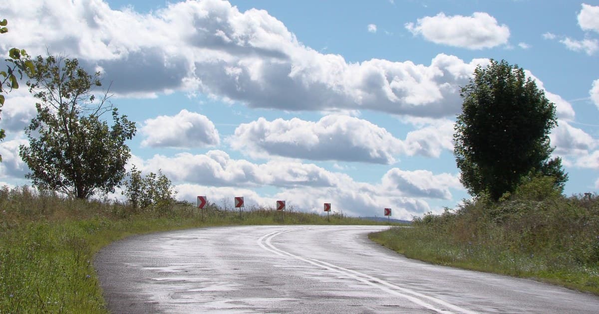 A picturesque rural road curves under a bright sky with fluffy clouds.
