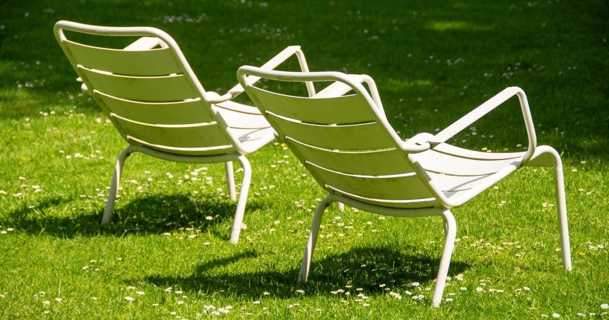 Two white metal chairs on a vibrant green lawn under sunlight.
